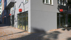 Fotomontage des von okamo aus Berlin gestalteten Designs für die Fassadengestaltung und Außenwerbung im Eckbereich des Gebäudes von „B18 Gesundheitszentrum Wilmersdorf“ in der Badenschen Straße 18 in Berlin mit den charakteristischen Farbwürfeln – bei Tag