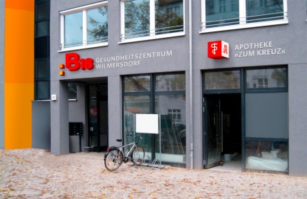 Fotomontage des von okamo aus Berlin gestalteten Designs für die Fassadengestaltung und Außenwerbung im Eingangsbereich von „B18 Gesundheitszentrum Wilmersdorf“ in der Badenschen Straße 18 in Berlin mit dem B18-Logo-Design und mit den charakteristischen Farbwürfeln – bei Tag